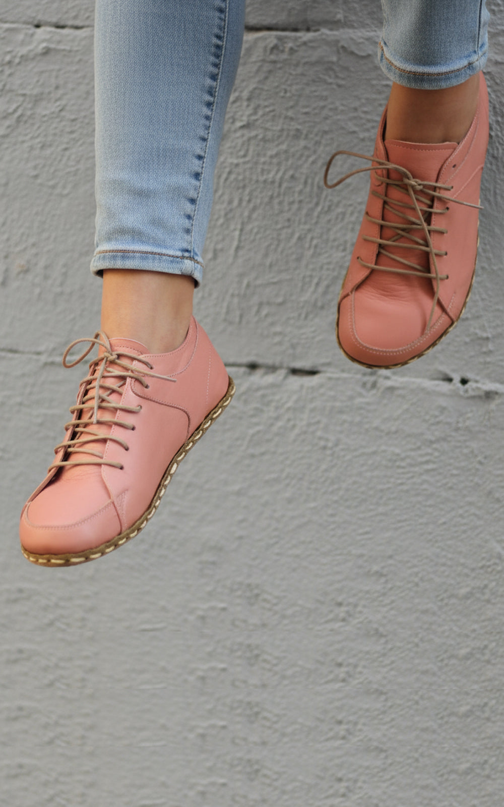 Pink shoes worn with light blue jeans against a gray concrete wall.